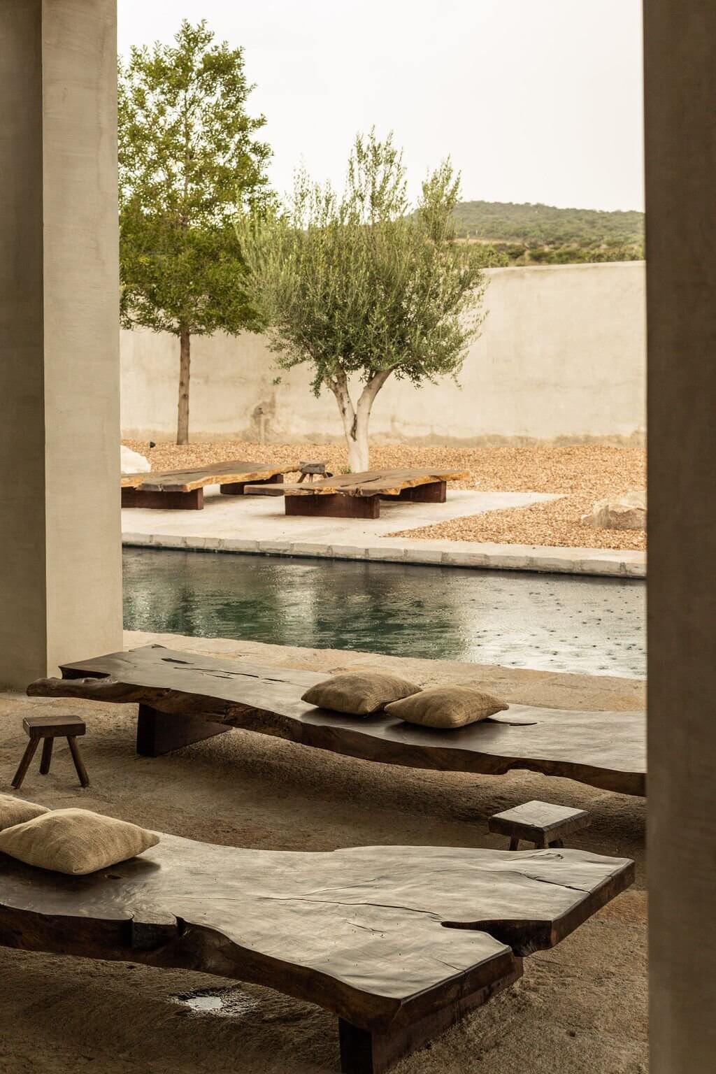 Villa ITO, Mexico — Concrete bench with linen pillows overlooking still pool, olive tree, and distant hills in minimalist courtyard.