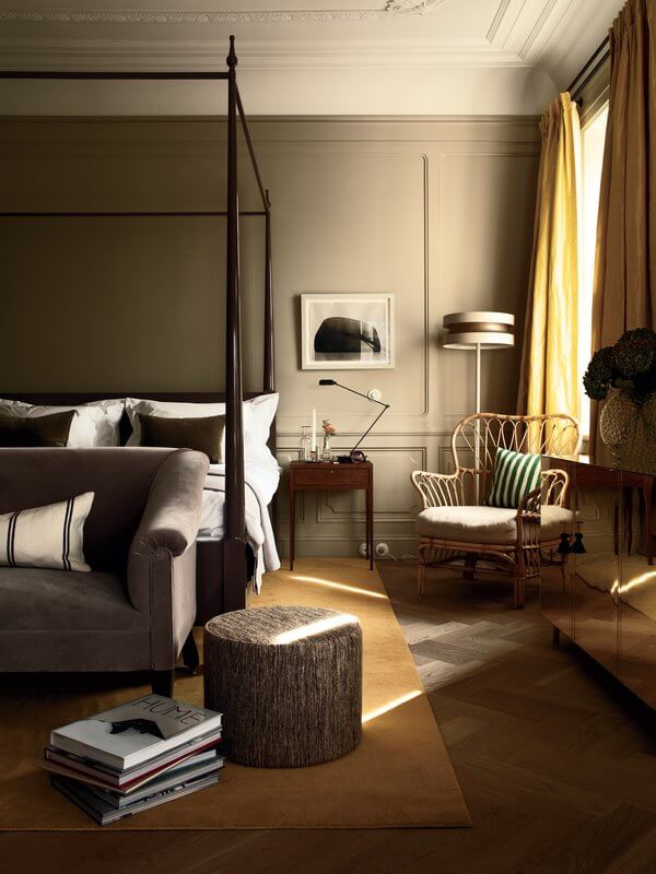Ett Hem, Europe — Canopy bed with dark frame in cream bedroom, rattan chair by window with yellow curtains, natural light, minimalist design, luxury hotel suite.