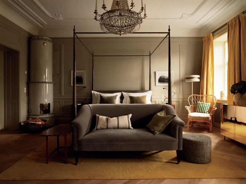 Ett Hem, Europe — Canopy bed with gray upholstered headboard, crystal chandelier, golden curtains, parquet floors, and classical architectural details in luxury hotel bedroom.