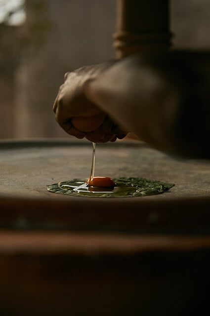 Paradero Todos Santos, Mexico — Hand drizzling amber honey over fresh herbs and tomato on stone plate, warm natural light casting soft shadows in minimalist dining setting.