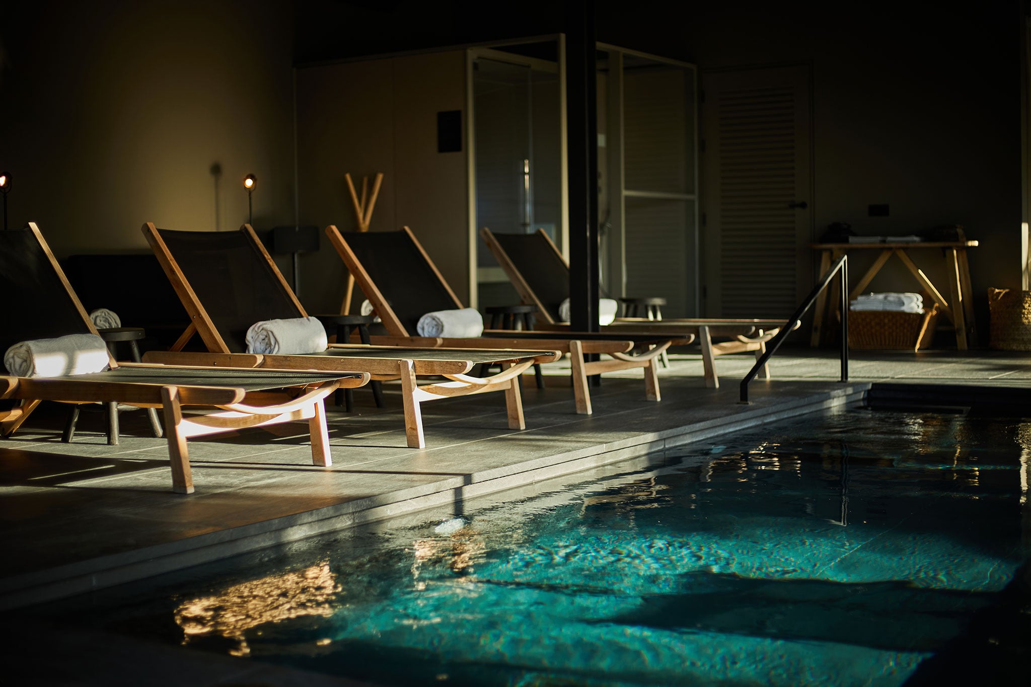 Único Spa, Balearic Islands, Spain — Nighttime poolside with wooden loungers, rolled towels, and turquoise water reflecting warm ambient lighting.