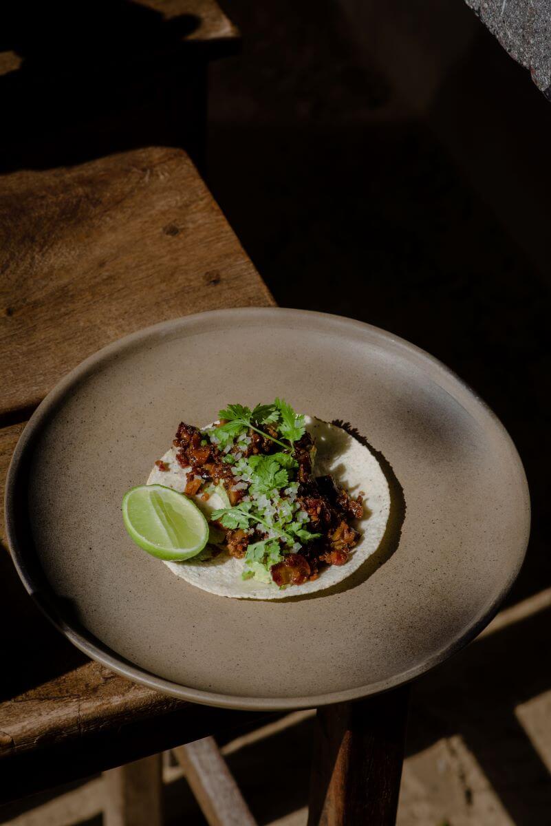 Paradero Todos Santos, Mexico — Plated taco with charred meat, crema, cilantro and lime on minimalist ceramic dish, warm natural light.