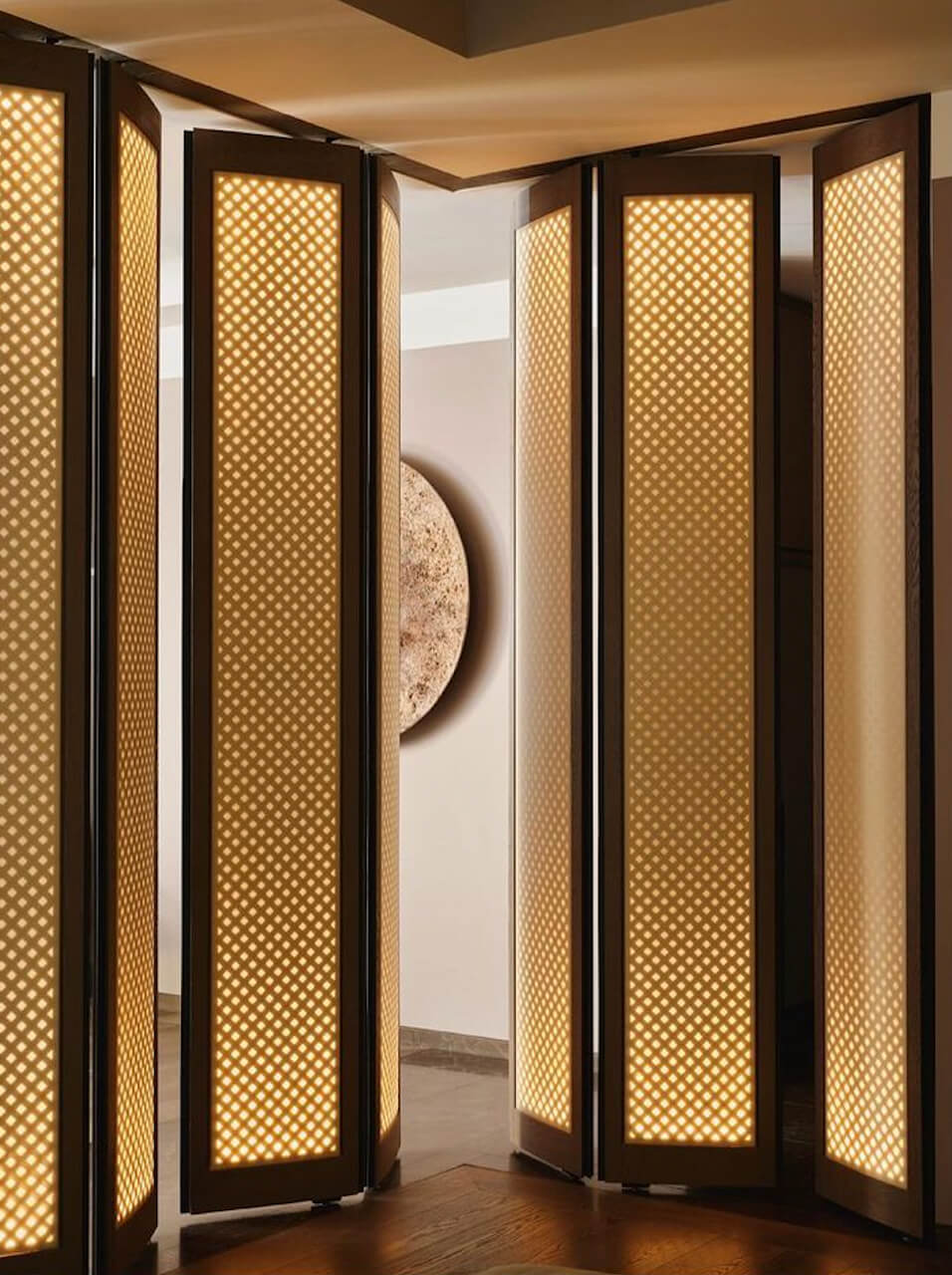 Aman New York, New York, USA — Illuminated brass mesh partition screens with black frames create layered ambient lighting in a minimalist corridor.