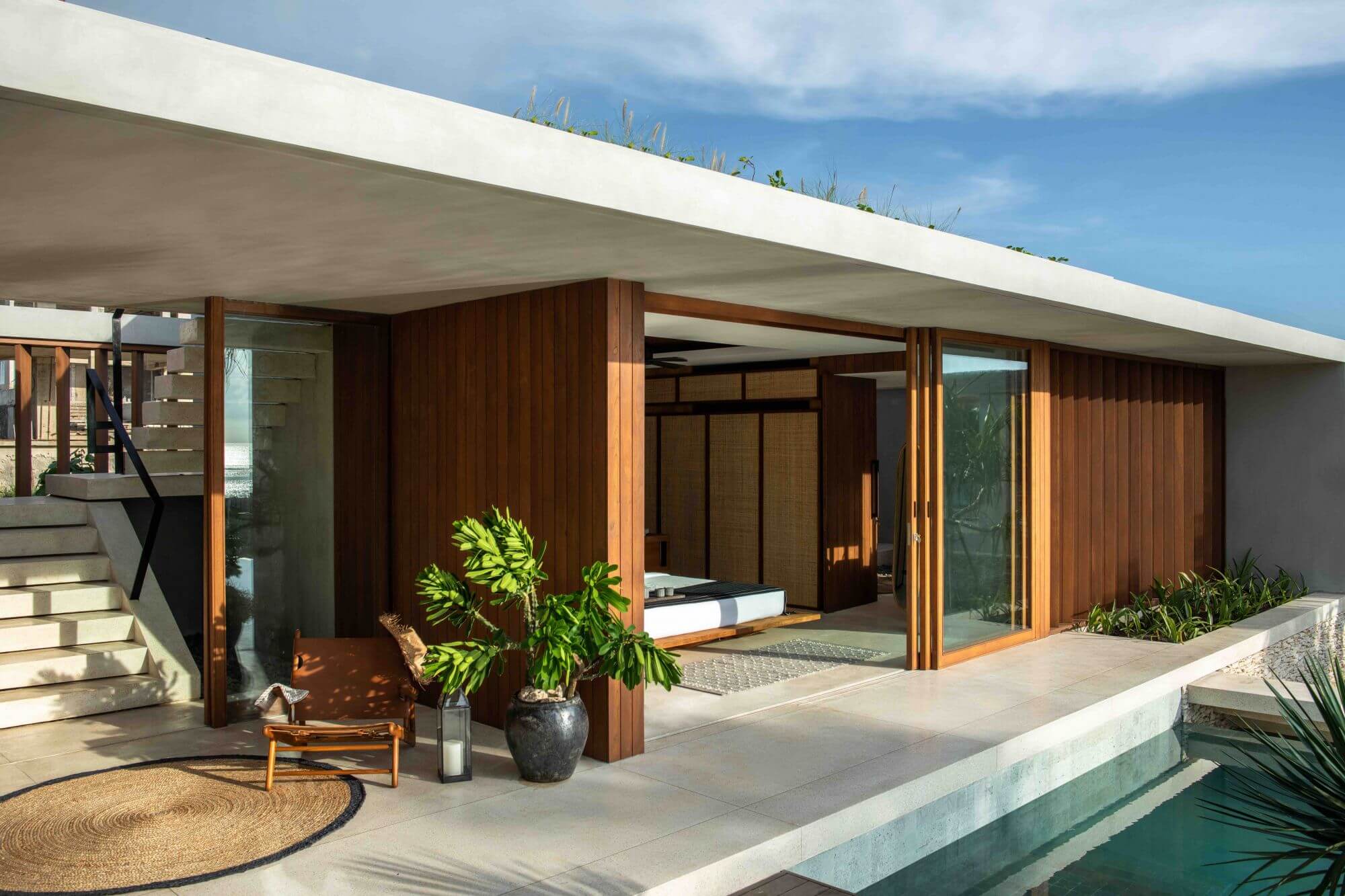 Cap Karoso, Asia — Modern pavilion with timber sliding doors, concrete roof terrace, sculptural planters, and infinity pool edge at dusk.