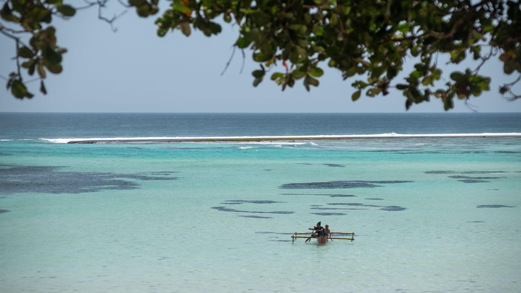 Cap Karoso, Asia — Outrigger canoe with passengers on turquoise lagoon waters, coral reefs visible, tropical foliage framing scene, reef break in distance.