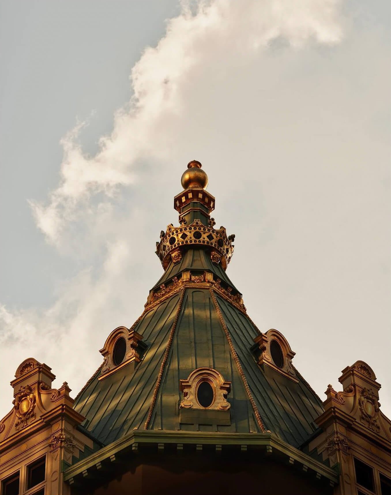 Aman New York, New York, United States — Gilded dome with green patina roof, ornamental bronze finials, and classical architectural details against clouded sky.