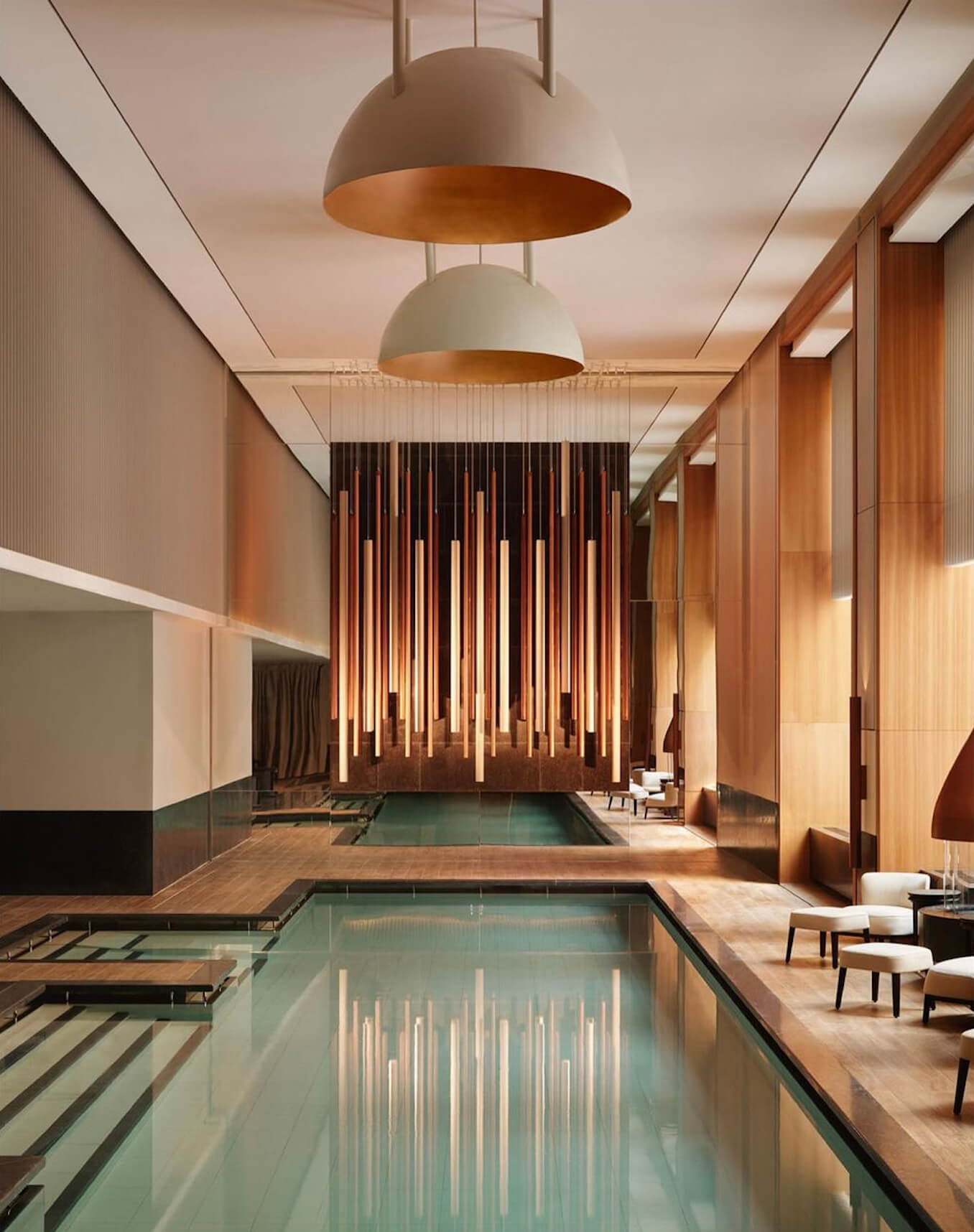 Aman New York, North America — Indoor lap pool with warm wood finishes, pendant lighting, and minimalist architectural detailing in luxury wellness spa.