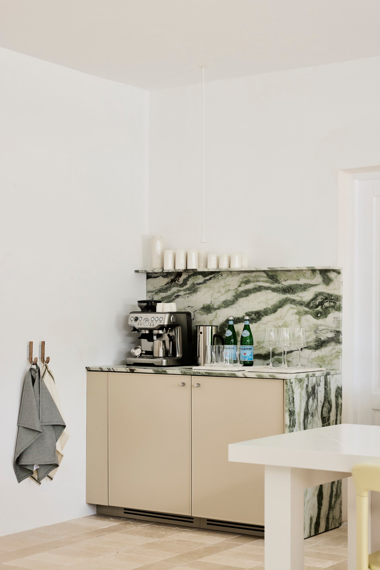 Villa Sessana, Italy — Minimalist kitchen bar with marble backsplash, cream cabinetry, espresso machine, and pendant candles overlooking dining area.