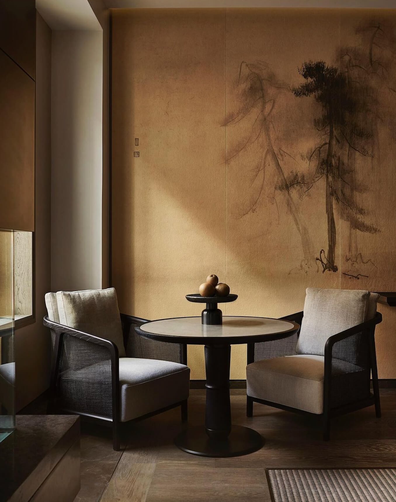 Aman New York, New York, United States — Minimalist lounge with ink-wash mural, paired black-framed chairs, round pedestal table, warm ochre walls, natural light.