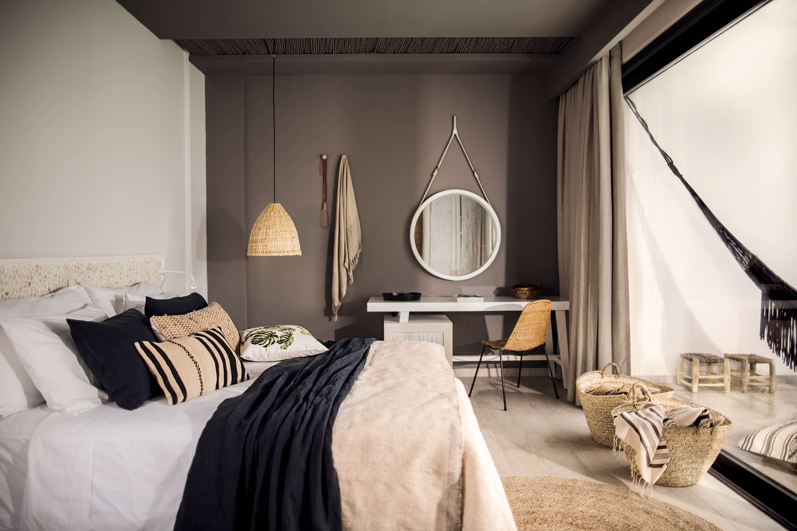 Casa Cook Rhodes, Europe — Minimalist bedroom with woven pendant lamp, striped pillows, circular mirror, natural linen textiles, rattan accents, and soft neutral palette.