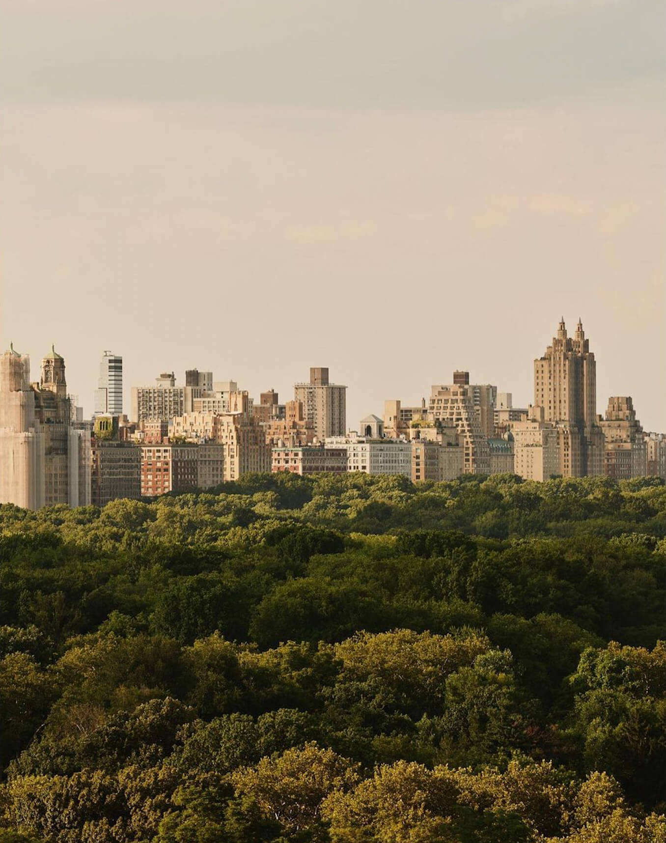 Aman New York, Manhattan, USA — Upper West Side skyline at golden hour with art deco spires rising above Central Park's dense canopy.