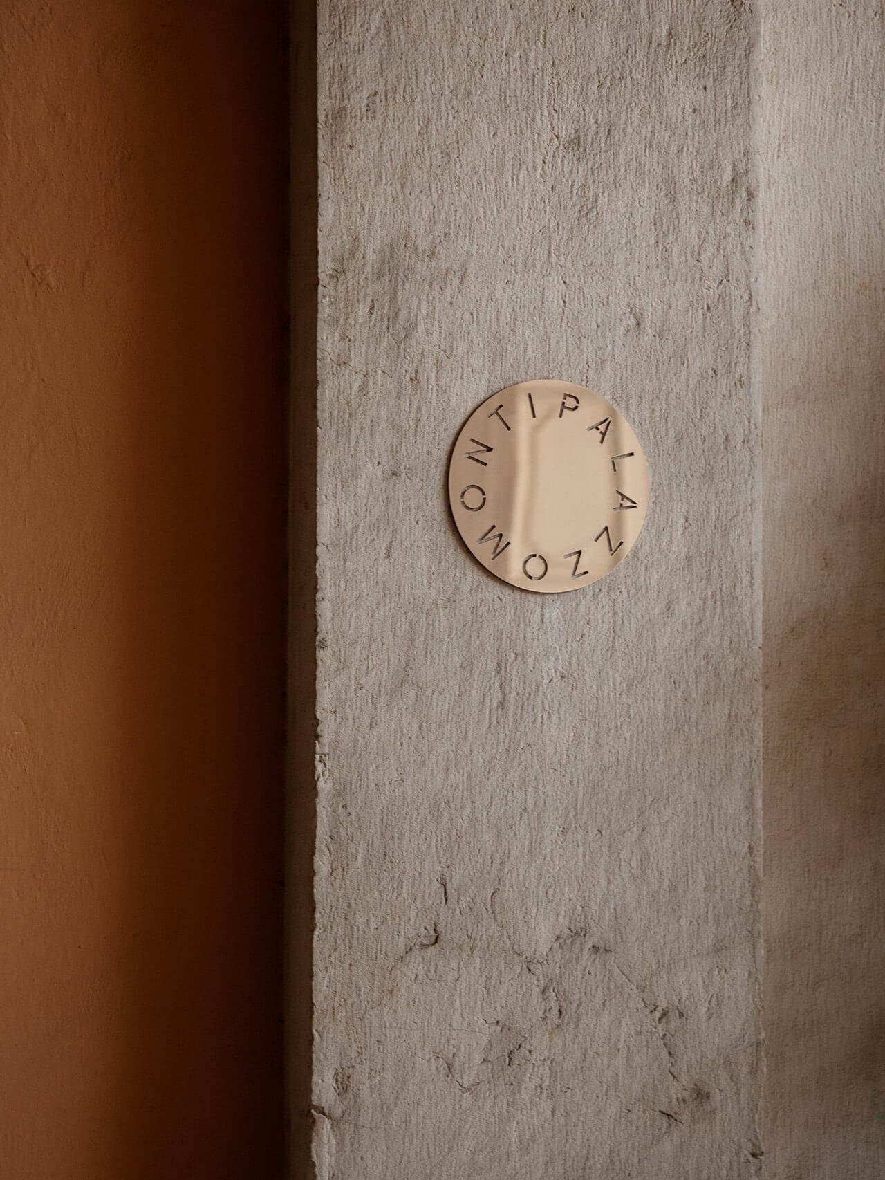 Vipp Palazzo Monti, Italy — Minimalist circular plaque with embossed typography on textured concrete wall beside warm terracotta panel, architectural detail.