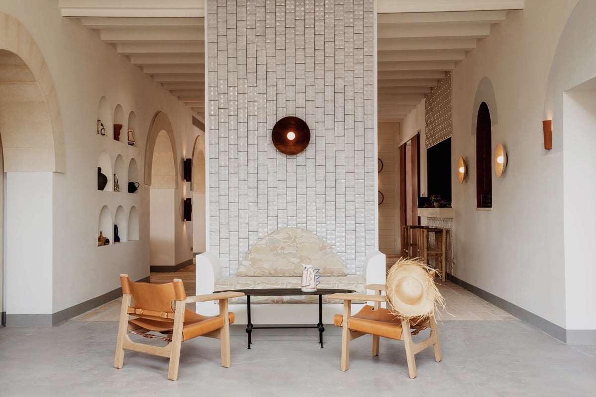 Menorca Experimental, Balearic Islands, Spain — Minimalist gallery space with arched alcoves, light wood chairs, concrete fireplace, and suspended copper pendant lighting.
