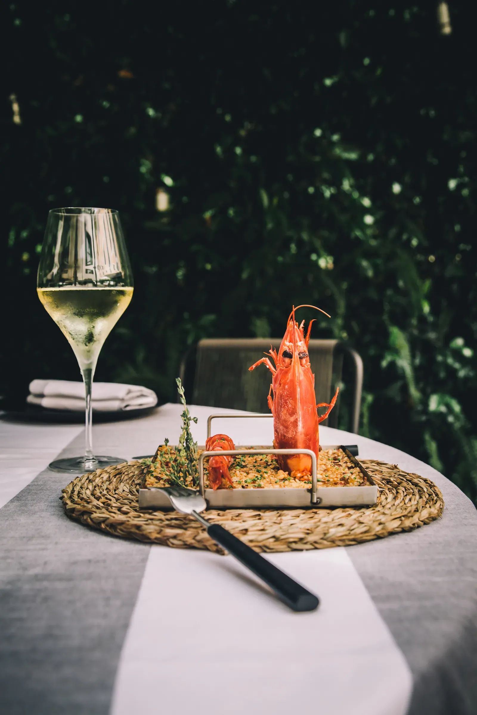 Sant Francesc Hotel Singular, Balearic Islands, Spain — White wine glass beside whole red langoustine on stone platter with herb garnish, lush green backdrop, fine dining table setting.