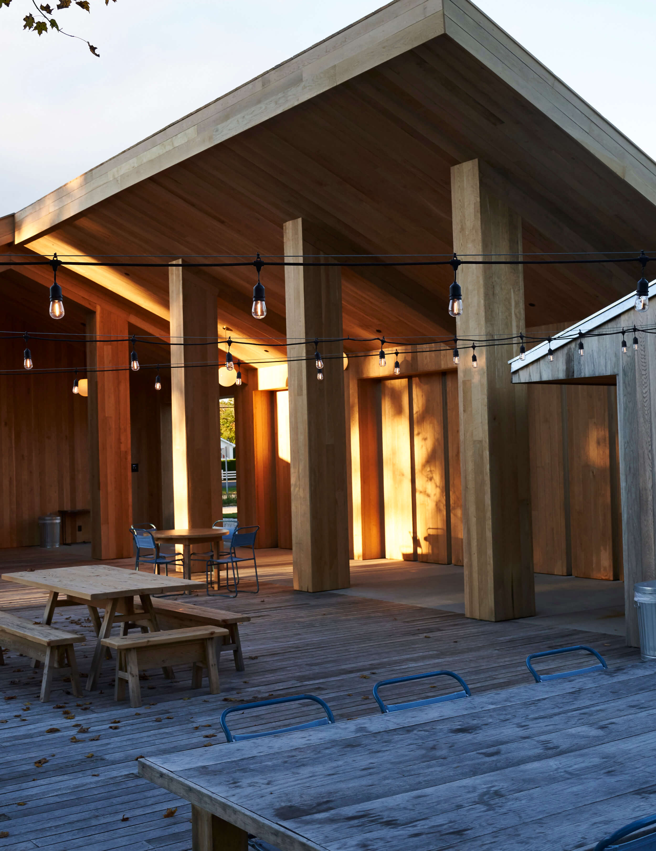 Tourists, North America — Modern pavilion with concrete columns, warm wood cladding, pendant lighting, and expansive deck at dusk.