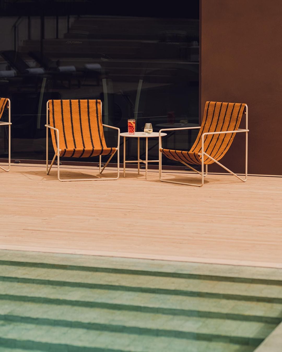 Aethos Ericeira, Portugal — Orange striped lounge chairs facing small table by pool, modernist design, coastal luxury hospitality aesthetic.