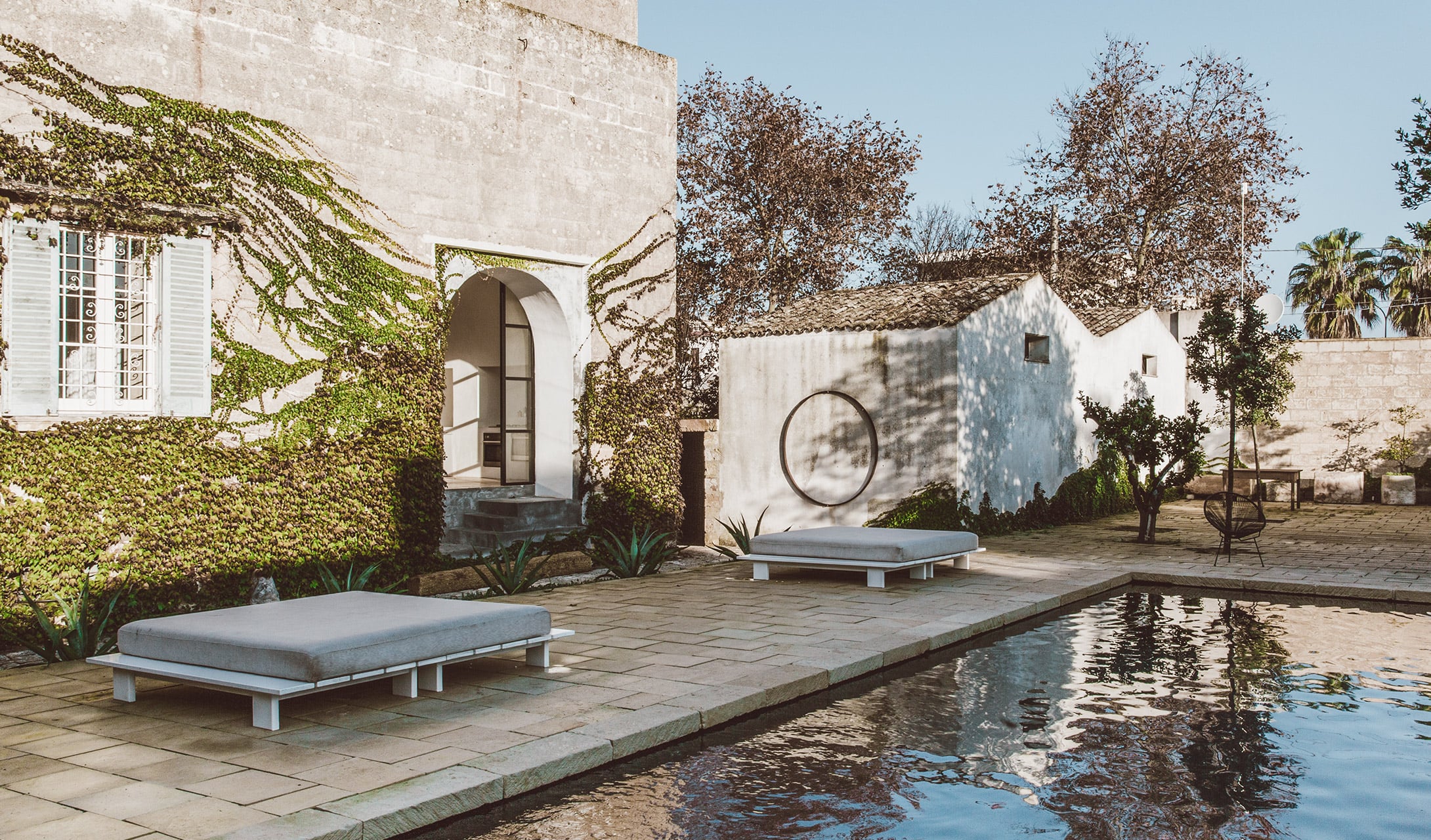 Palazzo’s Spa — Palazzo's Spa courtyard with whitewashed buildings, ivy-covered walls, minimalist loungers, circular swing, and reflecting pool under Mediterranean light.