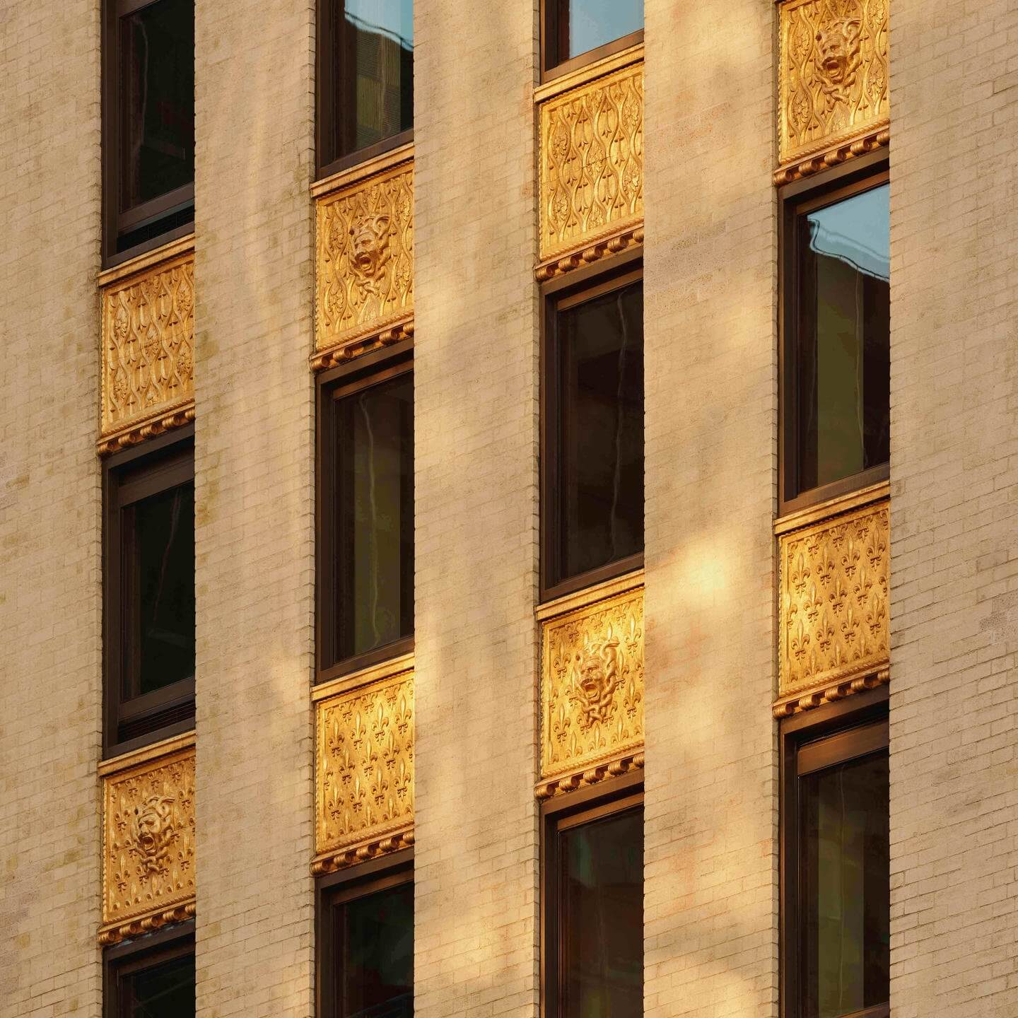 Aman New York, Manhattan, USA — Ornate gilt spandrels and dark wood-framed windows on a limestone facade, catching warm afternoon light.
