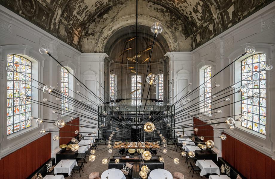 The Jane, Europe — Baroque vaulted ceiling with stained-glass windows, dramatic modern chandelier, white walls with red accents, symmetrical dining setup, contemporary luxury restaurant interior.