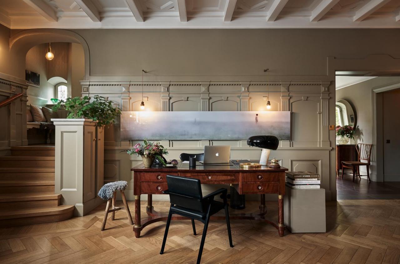Ett Hem, Europe — Timber desk in modernist office with arched doorways, coffered ceiling, and misty landscape artwork above paneled walls.
