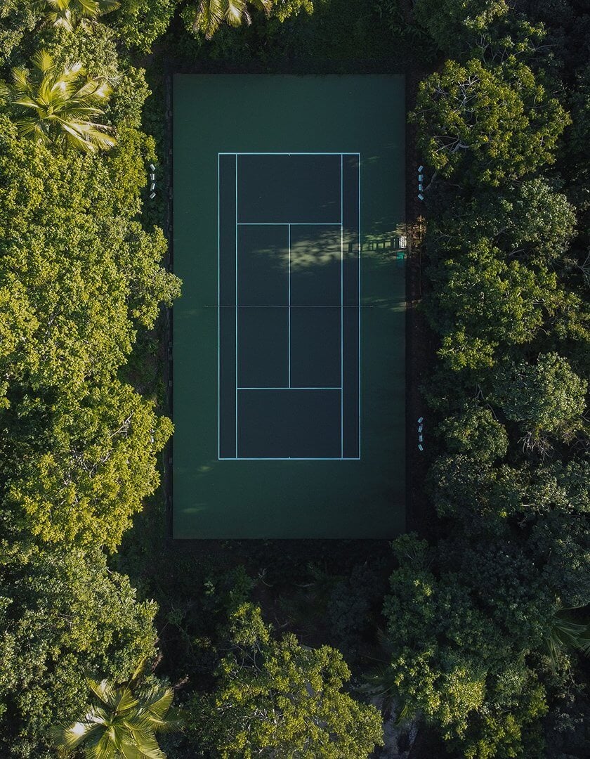 Barracuda Hotel & Villas, South America — Overhead view of tennis court nestled within dense tropical forest canopy, bright court lines against dark green surface surrounded by lush vegetation.