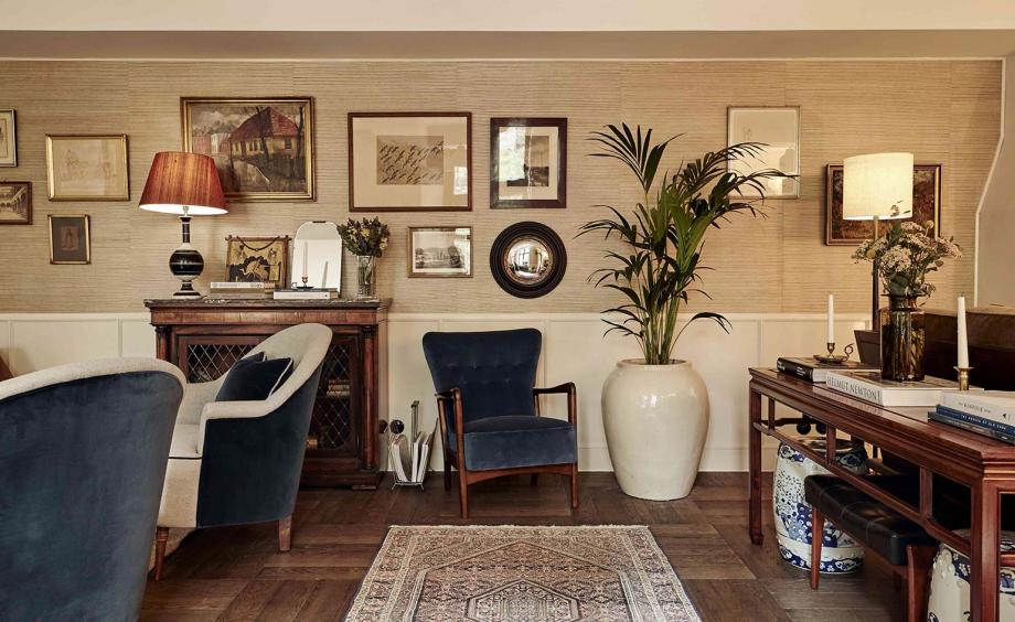 Hotel Sanders, Europe — Elegant sitting room with navy velvet chairs, wood paneling, fireplace mantel, gallery wall, potted plant, and warm ambient lighting.