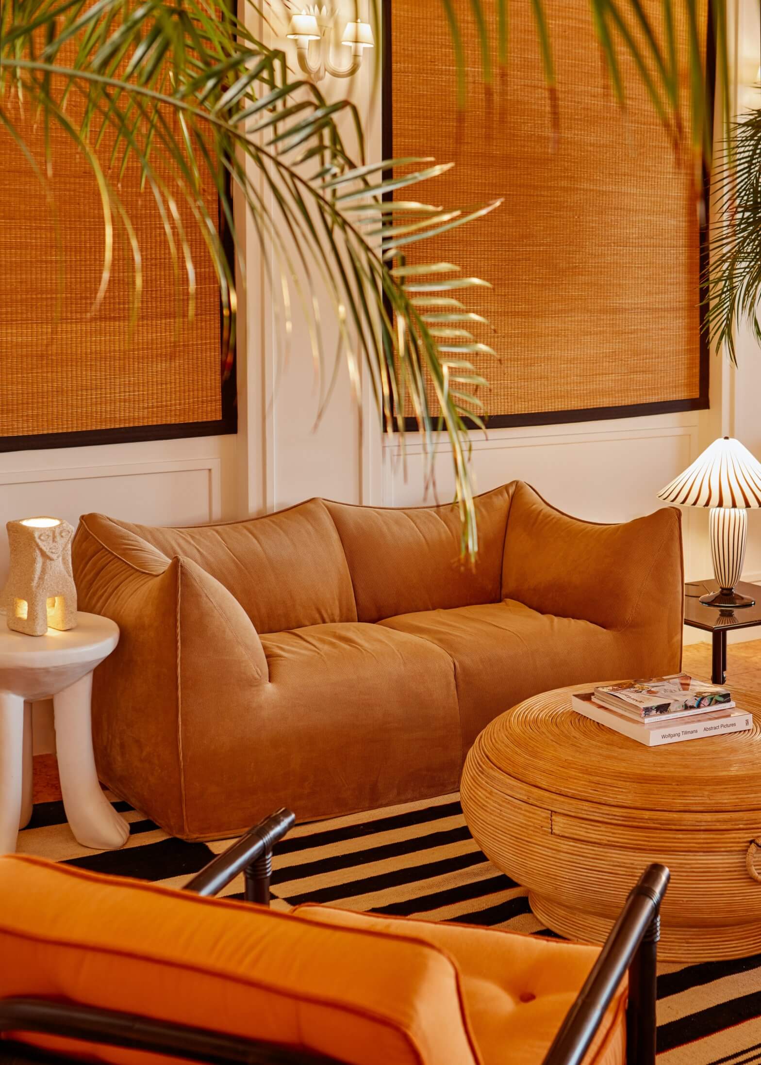 Palm Heights, North America — Cognac leather sofa with striped area rug, wooden side table, palm fronds, and orange linen panels in contemporary luxury lounge.