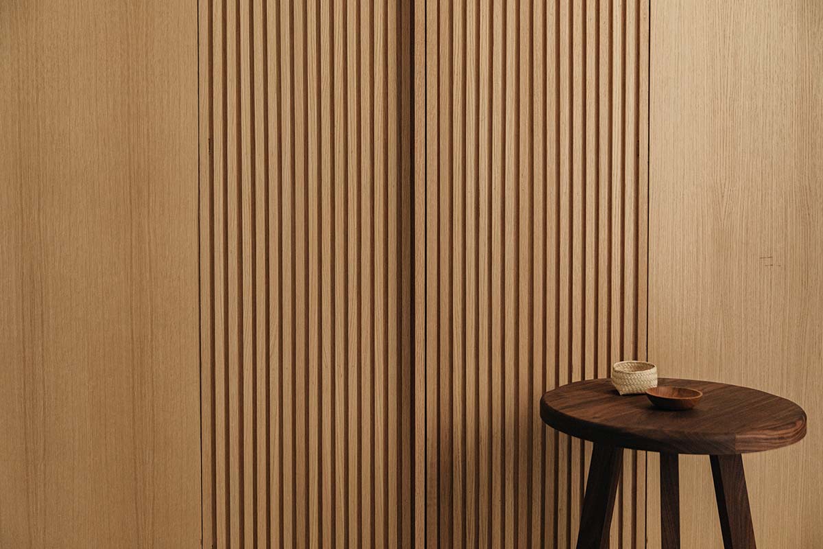 Octavia Casa, Mexico — Dark wooden side table with woven basket against warm wood-paneled wall with vertical fluting, minimalist hospitality interior design.