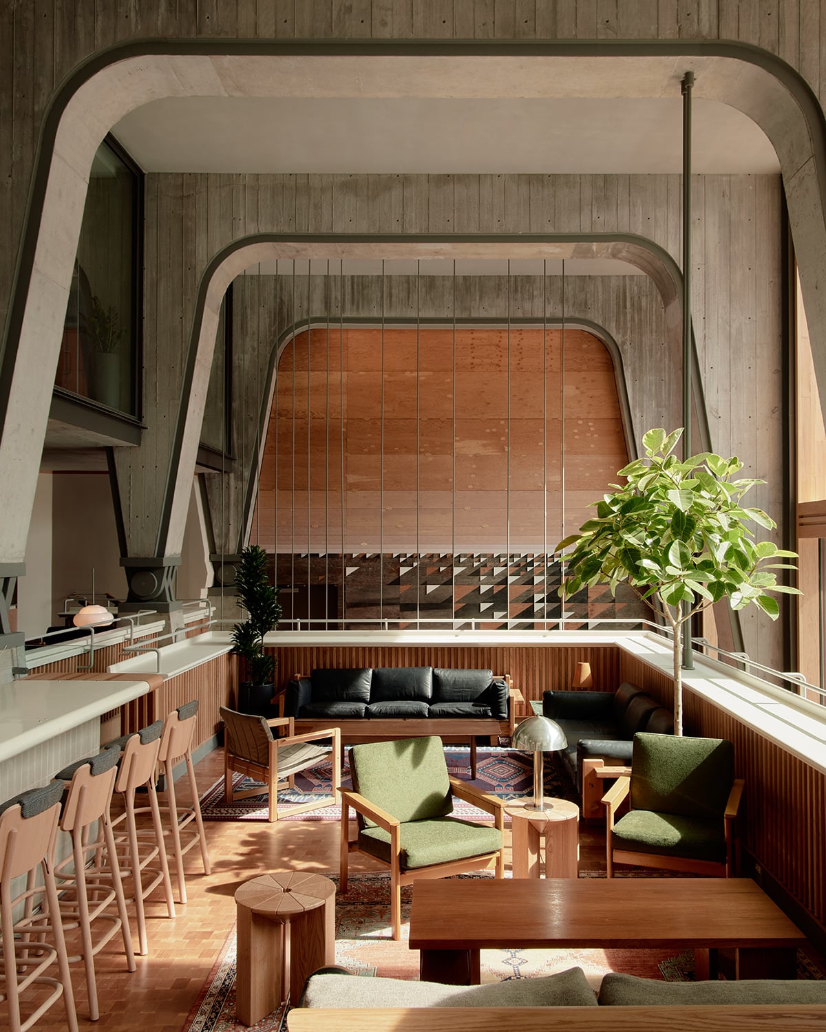Ace Hotel Toronto, Canada — Sunlit loft lounge with curved concrete archways, wooden furnishings, green upholstered chairs, and floor-to-ceiling windows overlooking city views.
