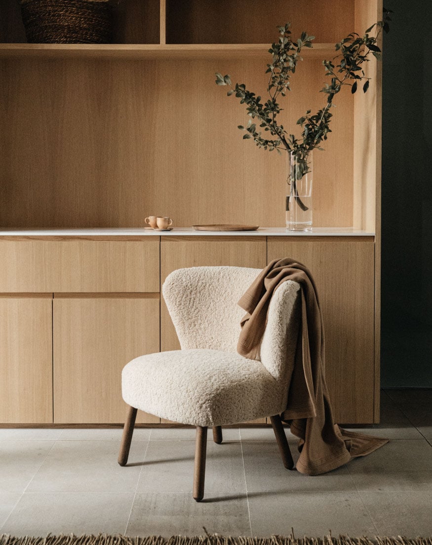 Octavia Casa, Mexico — Cream boucle chair with wooden legs beside natural wood cabinetry, dried botanicals in glass vase, minimalist hospitality interior design.