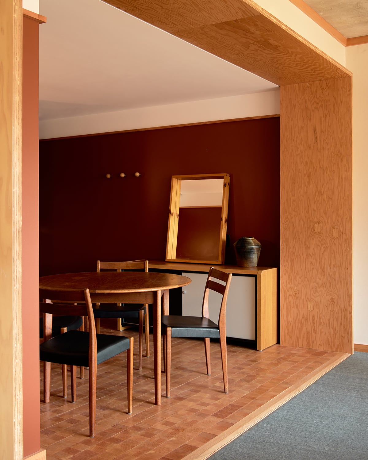 Ace Hotel Toronto, Canada — Mid-century dining nook with burgundy accent wall, round wood table, leather chairs, and brass hardware reflecting modernist hospitality design.