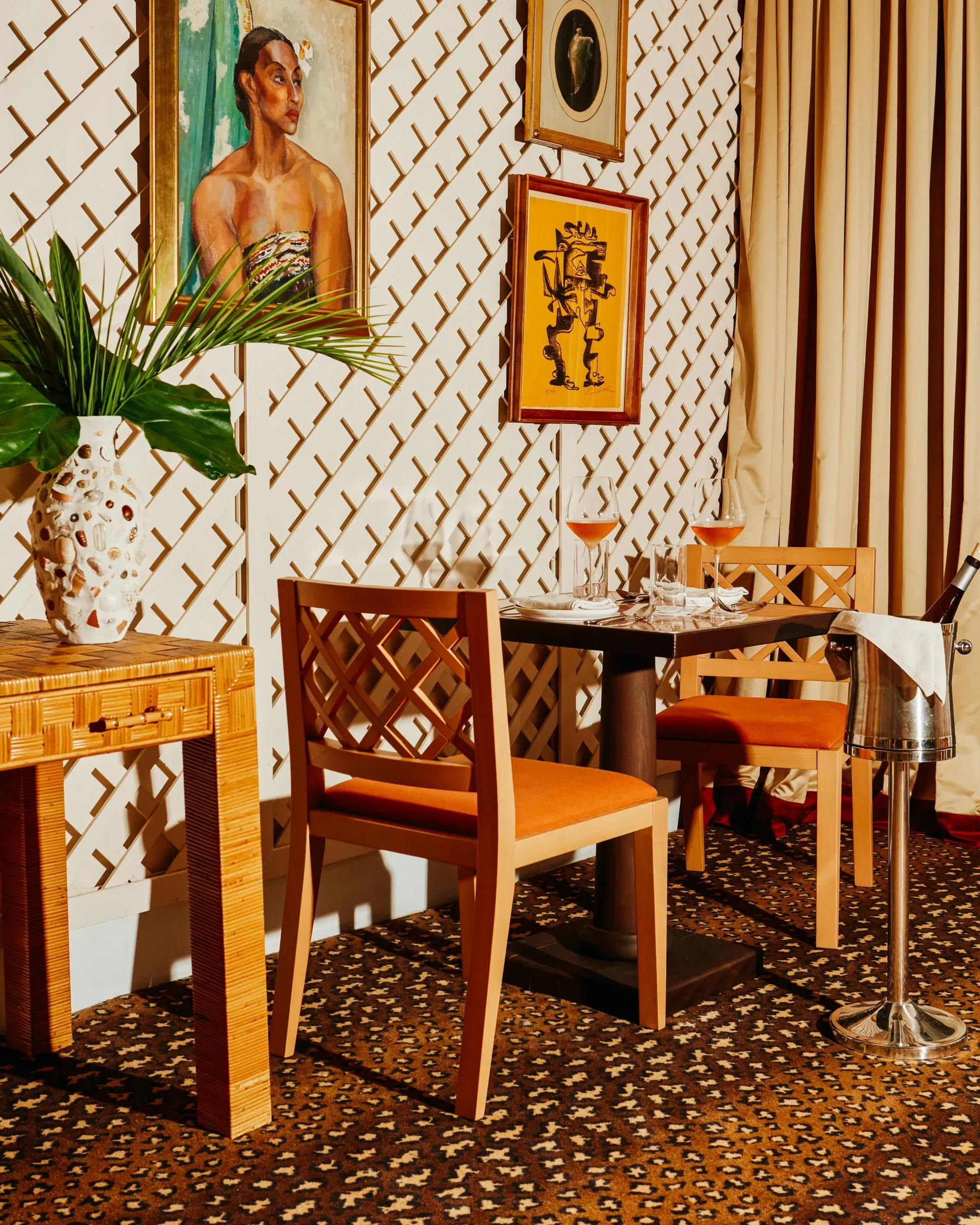 Palm Heights, North America — Dining room with geometric wood chairs, patterned wallpaper, framed artwork, tropical plant, and warm amber lighting creating intimate luxury interior.