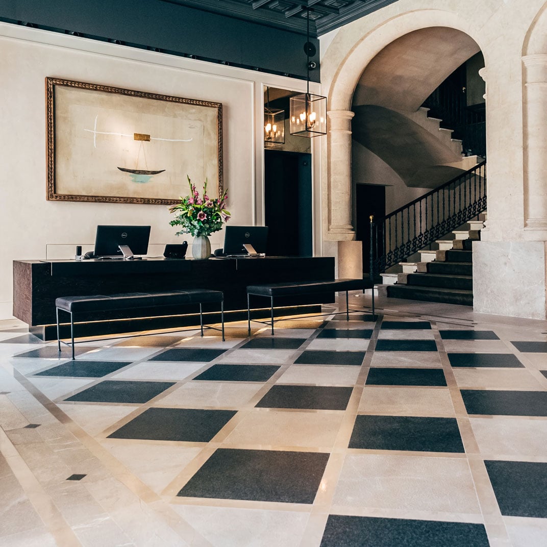 Sant Francesc Hotel Singular, Balearic Islands, Spain — Minimalist lobby with geometric stone floor, black reception desk, spiral staircase, and modernist wall art beneath teal ceiling.