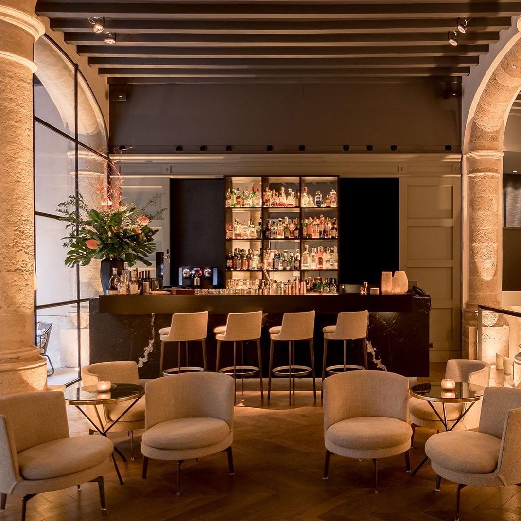 Sant Francesc Hotel Singular, Balearic Islands, Spain — Illuminated bar with backlit liquor display, cream upholstered seating, stone archways, and warm ambient lighting in luxury hospitality lounge.