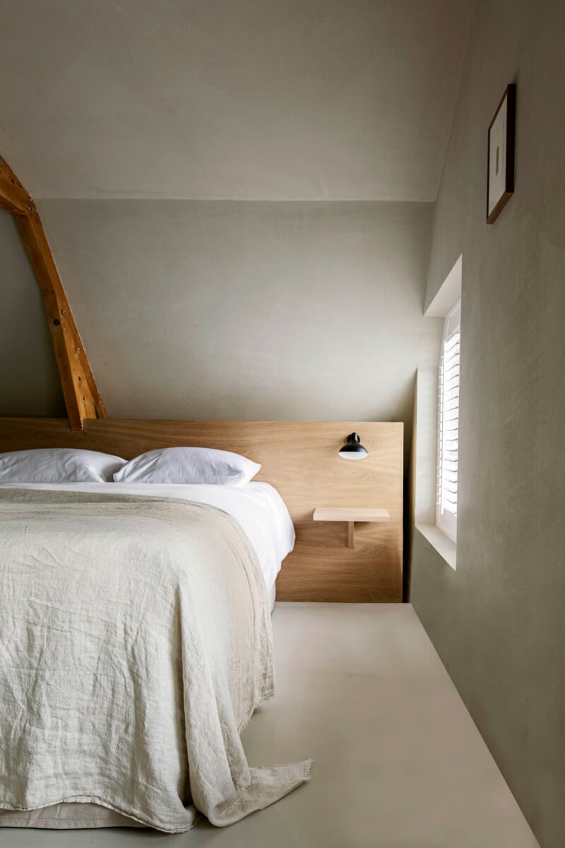 Hotel âme, Europe — Minimalist bedroom with natural light, wooden bed frame, white linens, neutral walls, and clean architectural lines.