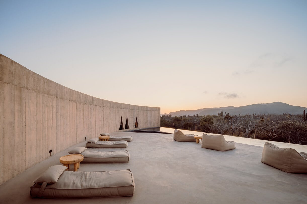 Ojo de Agua Spa, Mexico — minimalist concrete rooftop with linen seating, mountain views at sunset, modernist wellness architecture.