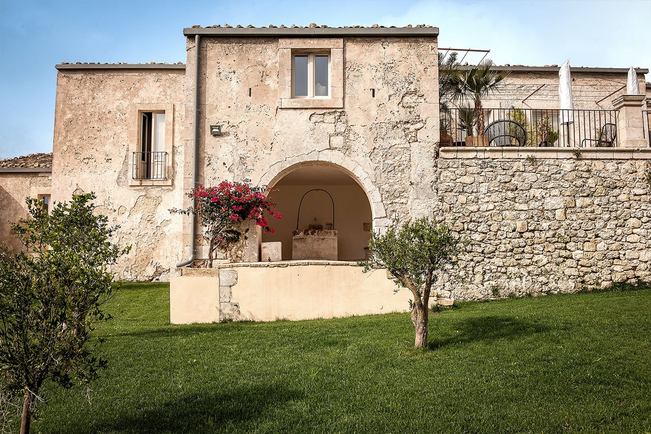 Dimora delle Balze, Europe — Stone archway with magenta bougainvillea, weathered limestone facade, manicured lawn, Mediterranean luxury architecture.