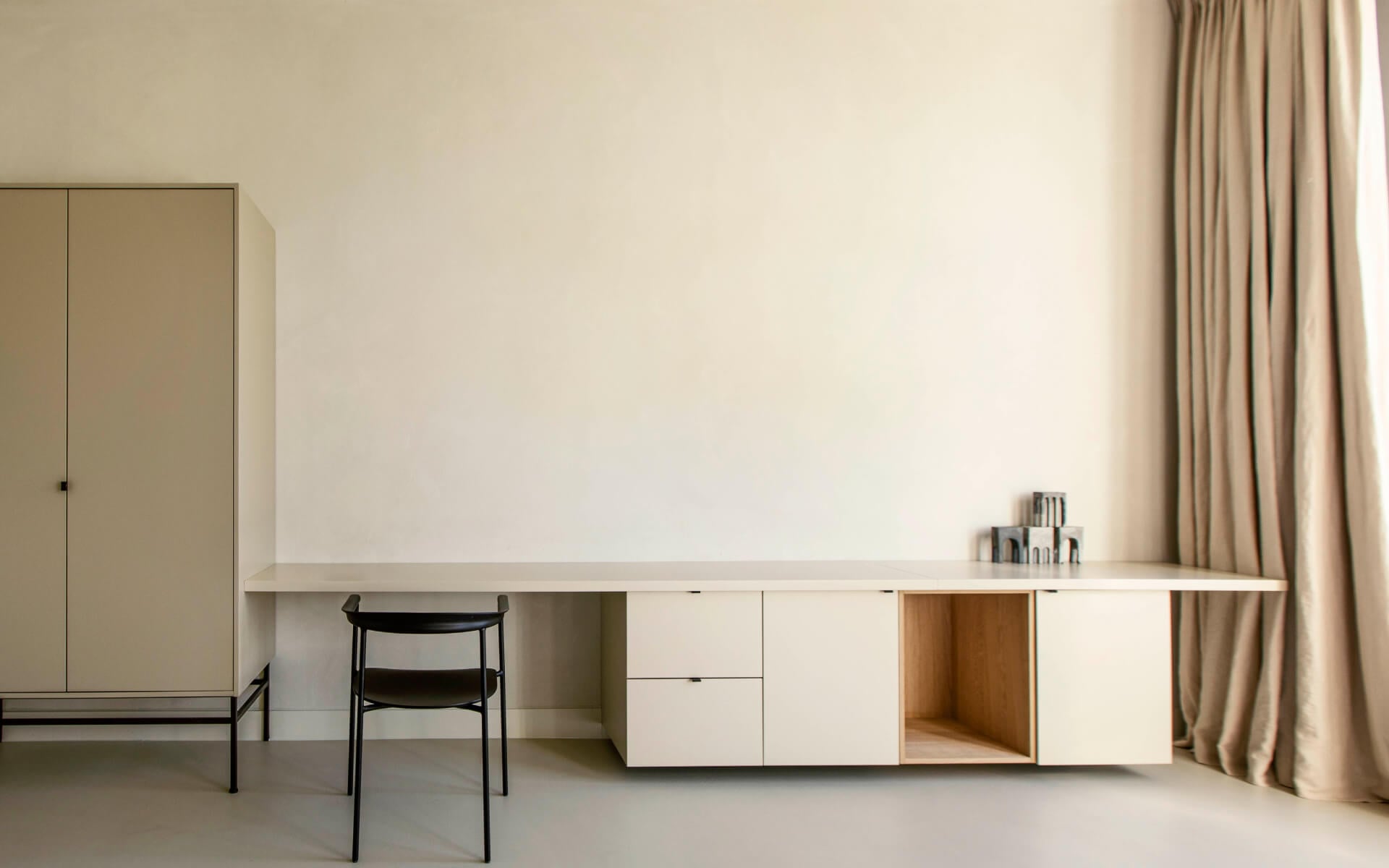 Hotel âme, Europe — Minimalist workspace with white cabinetry, natural wood accents, black chair, and floor-to-ceiling curtains in serene neutral tones.
