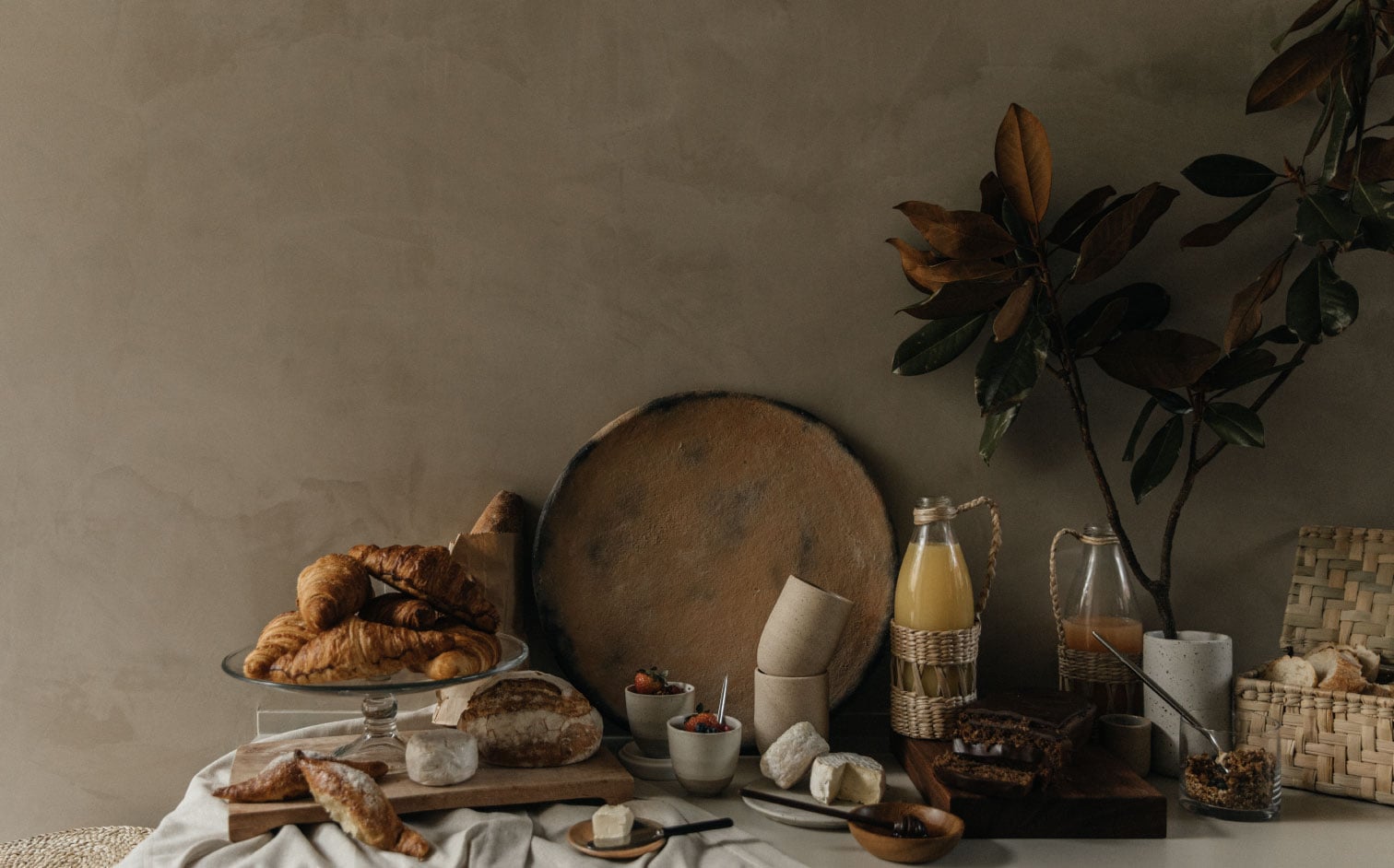 Octavia Casa, Mexico — Styled breakfast table with croissants, bread, ceramics, and glassware against neutral wall with dried botanicals and natural light.