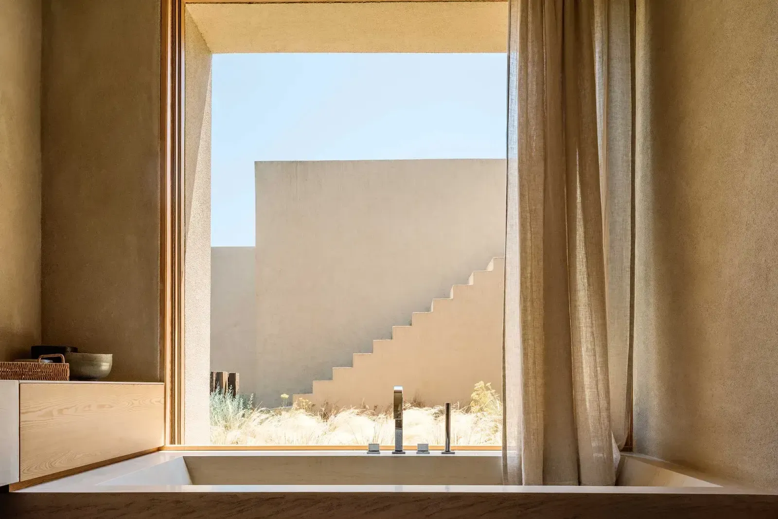 Melides Art, Portugal — Minimalist bathroom with concrete soaking tub overlooking stepped architectural facade and desert landscape under clear sky.