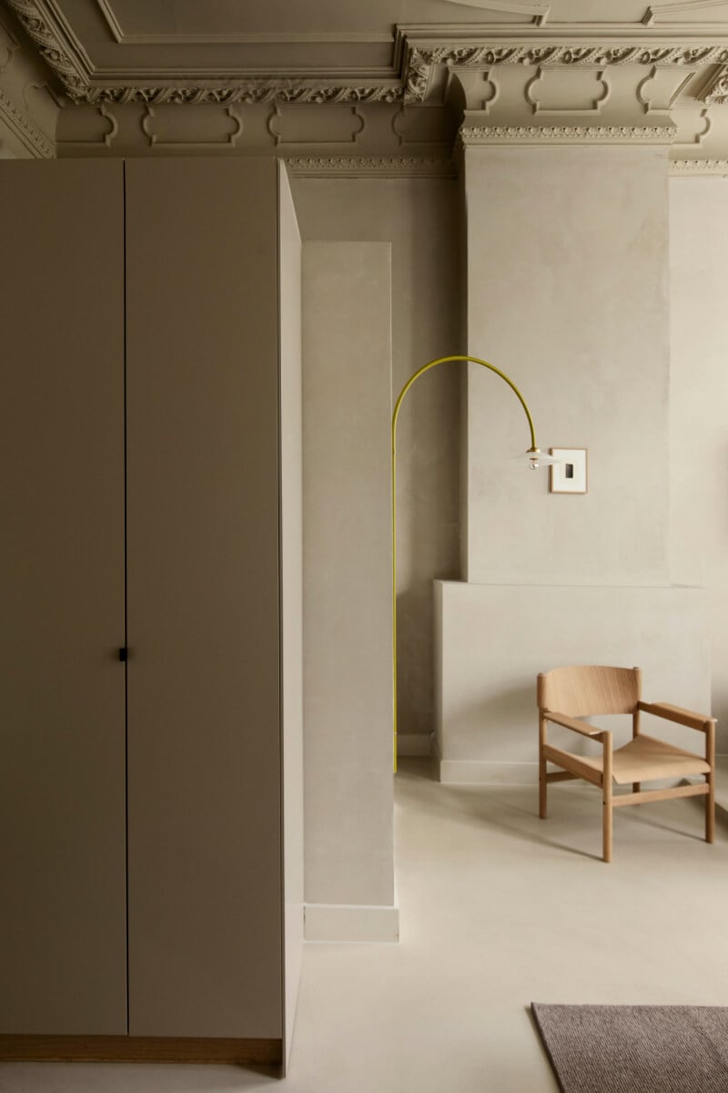 Hotel âme, Europe — Minimalist interior with ornate ceiling molding, yellow arc floor lamp, natural wood chair, and neutral plaster walls creating refined spatial composition.