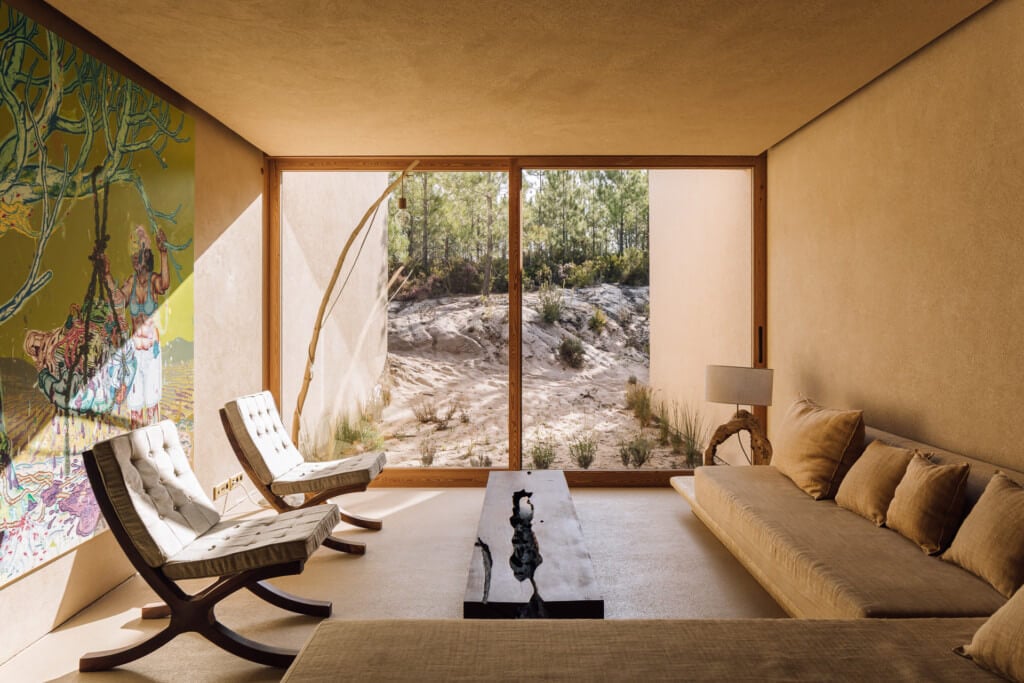 Melides Art, Portugal — Minimalist interior with terracotta walls, modernist furniture, large windows overlooking rocky landscape and pine forest, contemporary art installation.