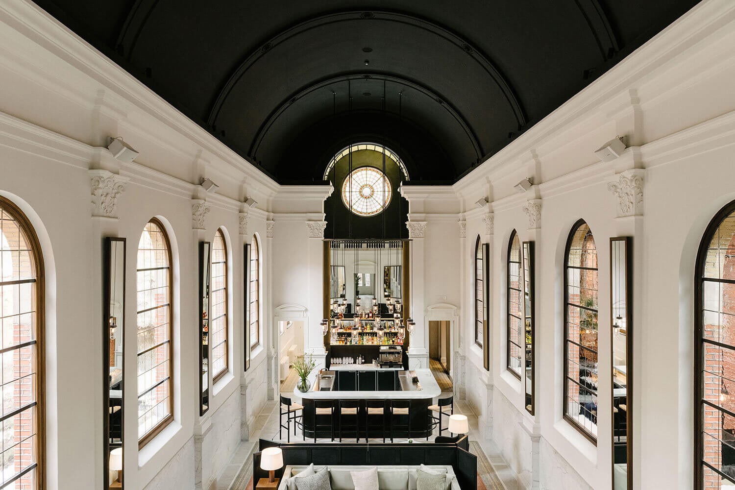 August, Europe — Barrel-vaulted corridor with white marble walls, arched windows, central bar counter, and illuminated clock, luxury hospitality design.