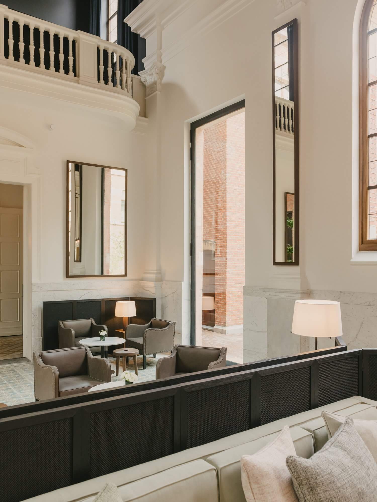 August, Europe — Cream and black interior with soaring ceilings, marble accents, taupe seating, and tall windows overlooking brick architecture.