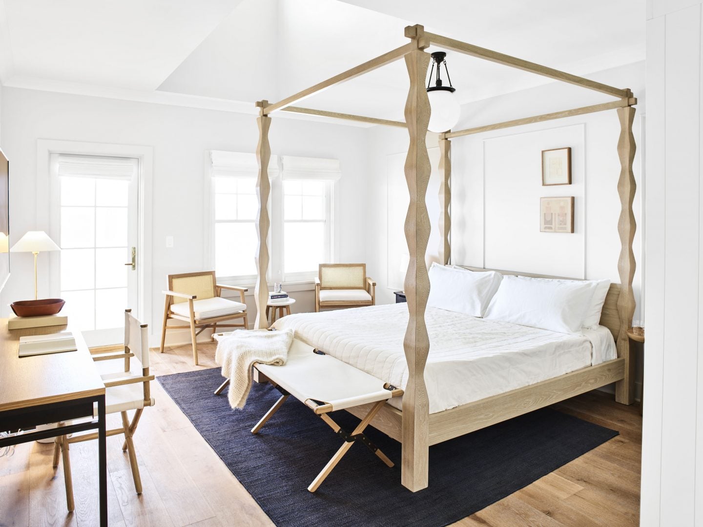 The Lake House, North America — Light oak canopy bed with twisted posts, white linens, and brass hardware in minimalist bedroom with natural light and mid-century furniture.