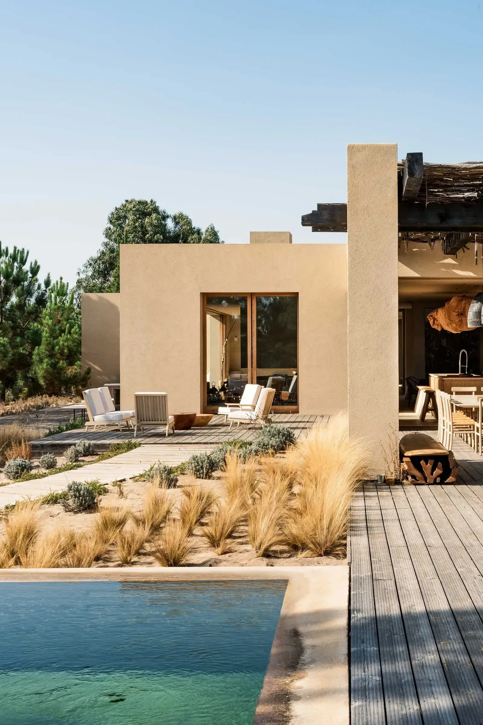 Melides Art, Portugal — Minimalist stucco villa with wooden deck, pool, and ornamental grasses in Mediterranean landscape.