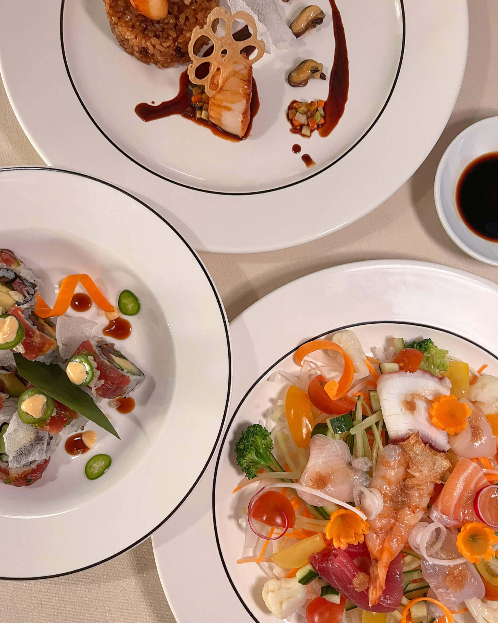 Yashinoki, North America — Fine dining plated dishes with sashimi, seared protein, and vegetable garnish on white rimmed plates with dark borders, soft natural lighting.