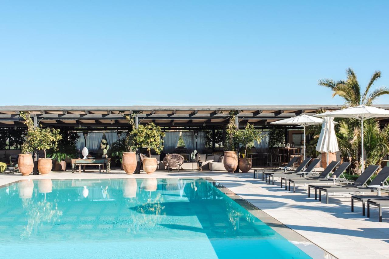 Dimora delle Balze, Europe — Turquoise poolside terrace with terra-cotta urns, pergola, loungers, umbrellas, and palm trees under clear sky.