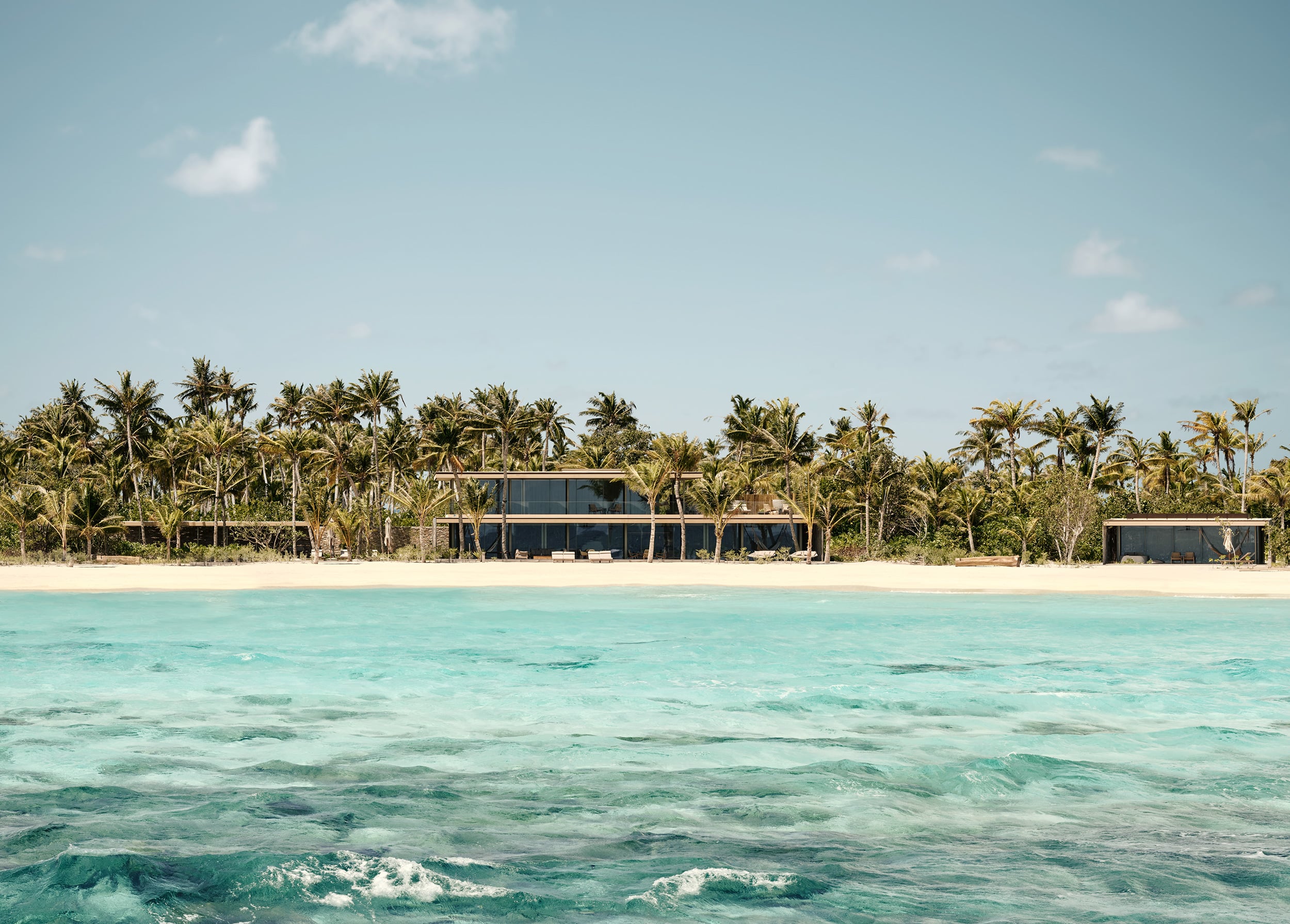 Patina Maldives, Asia — Modernist beachfront residence with floor-to-ceiling glass, dark timber accents, and coconut palms overlooking turquoise lagoon at sunset.