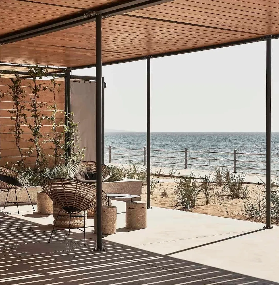 Dexamenes Seaside Hotel, Europe — Modern beachfront pavilion with wooden slatted ceiling, floor-to-ceiling glazing, woven lounge chairs, and unobstructed sea views.